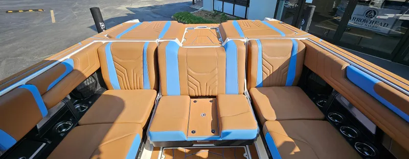 Slide: The Image of 2025 Malibu 25LSV boat interior with tan and blue seating, cup holders, and modern design. - 16
