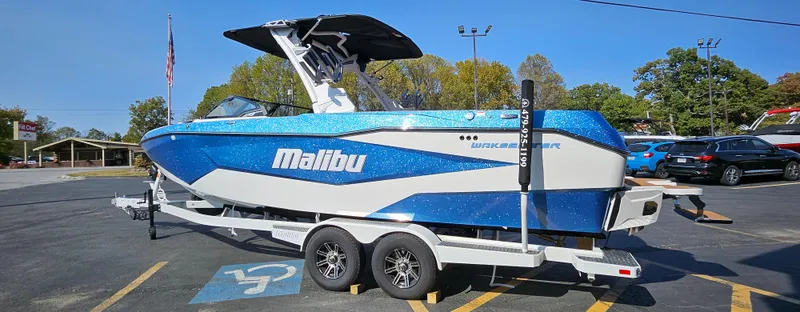 Slide: The Image of 2025 Malibu 25LSV boat on trailer, blue and white design, parked outdoors. - 2