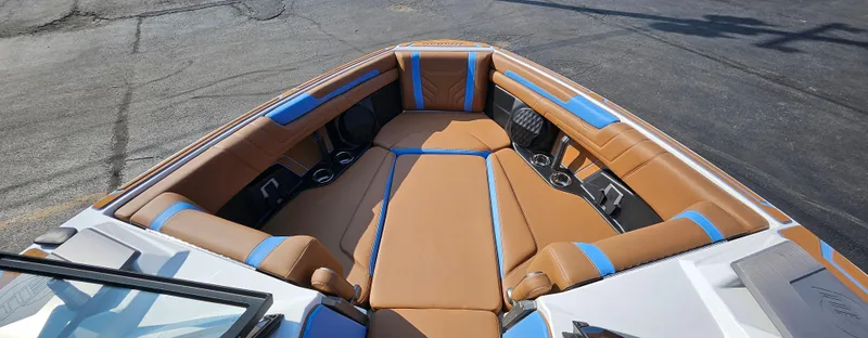Slide: The Image of 2025 Malibu 25LSV boat interior with tan and blue seating, cup holders, and sleek design. - 24
