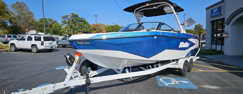 Slide: The Image of 2025 Malibu 25LSV boat on trailer in parking lot, blue and white design. - 4