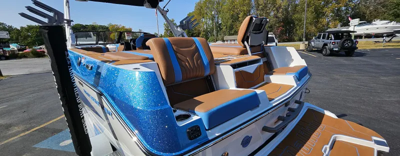 Slide: The Image of 2025 Malibu 25LSV boat with blue and brown seating, parked outdoors. - 7