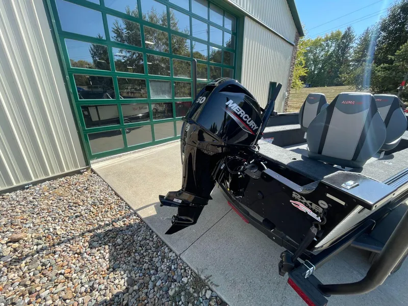 Slide: The Image of 2024 Alumacraft Classic 165 Tiller boat with Mercury engine, parked outside a garage. - 3