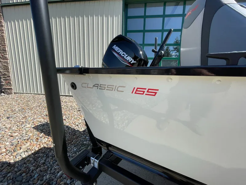 Slide: The Image of 2024 Alumacraft Classic 165 Tiller boat with Mercury engine, parked outdoors. - 5