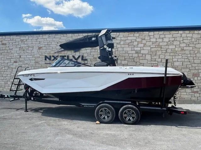 Slide: The Image of 2022 Nautique G23 boat on trailer, parked outdoors against stone wall. - 1