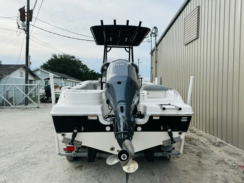 Slide: The Image of 2022 NauticStar 2102 Legacy boat with outboard motor, parked near a metal building. - 14