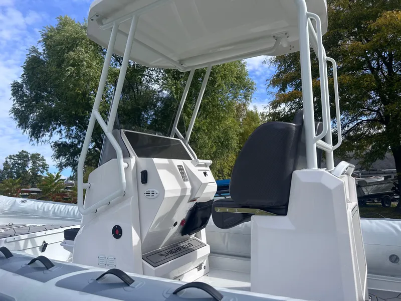 Slide: The Image of 2024 Highfield Sport 660 boat interior with console and seating, surrounded by trees. - 7