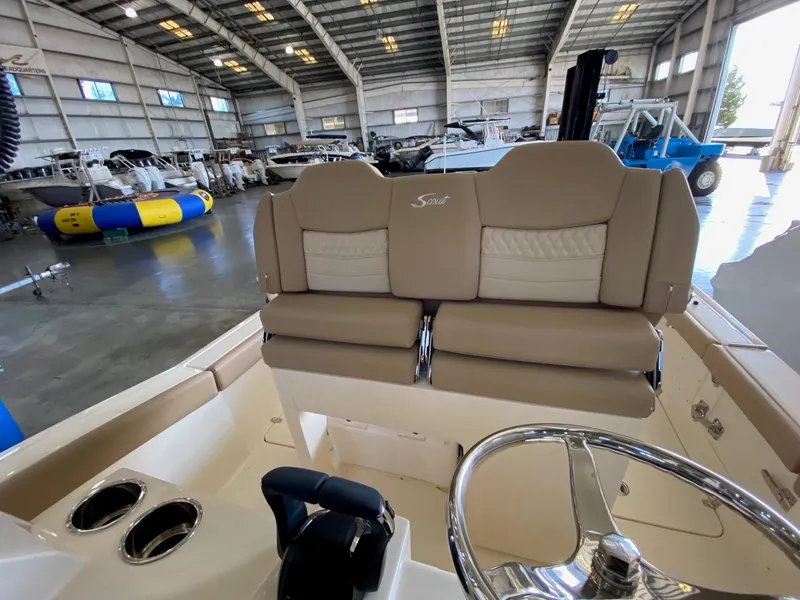 Slide: The Image of 2025 Scout 260 LXF boat interior with beige seating in a spacious warehouse. - 12
