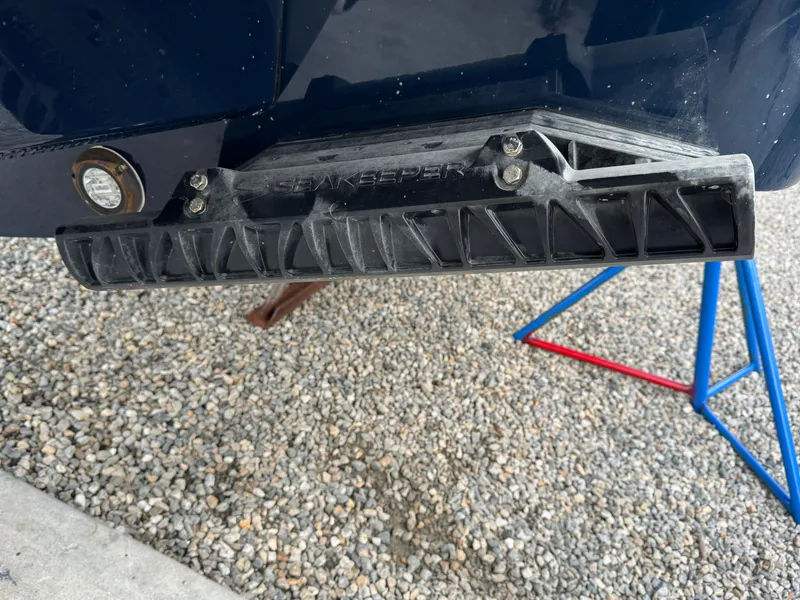 Slide: The Image of 2025 Regulator 31 boat detail showing a black trim tab on gravel surface. - 3