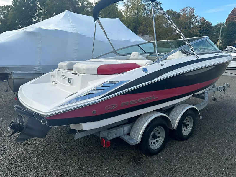 Slide: The Image of 2011 Regal 2100 Bowrider boat on trailer, white and red design, parked outdoors. - 2
