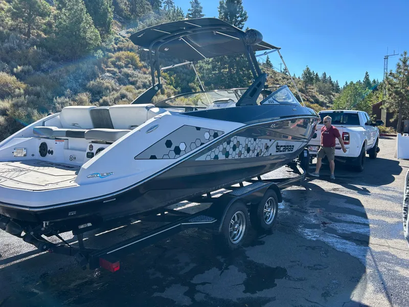 Slide: The Image of 2019 Scarab 255 ID boat on trailer, parked outdoors near trees and a white truck. - 13