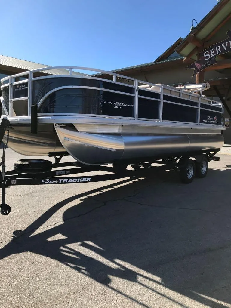 Slide: The Image of 2025 Sun Tracker Fishin' Barge 20 DLX pontoon boat on trailer, outdoor setting. - 2