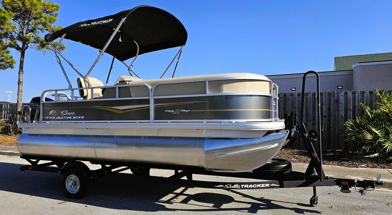 Slide: The Image of 2025 Sun Tracker Party Barge 18 DLX pontoon boat on trailer, parked outdoors. - 2