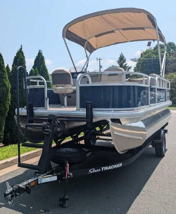 Slide: The Image of 2025 Sun Tracker Bass Buggy 18 DLX pontoon boat on trailer, outdoor setting. - 2