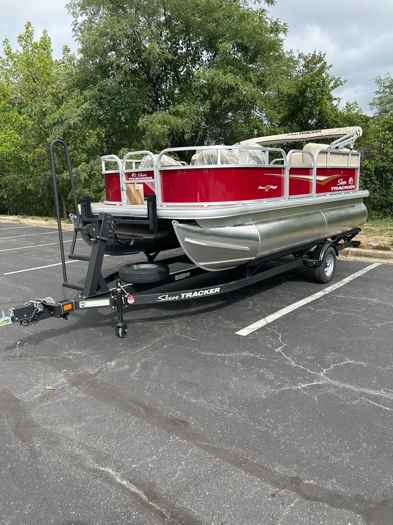 Slide: The Image of 2025 Sun Tracker Bass Buggy 16 XL Select pontoon boat on trailer in parking lot. - 2