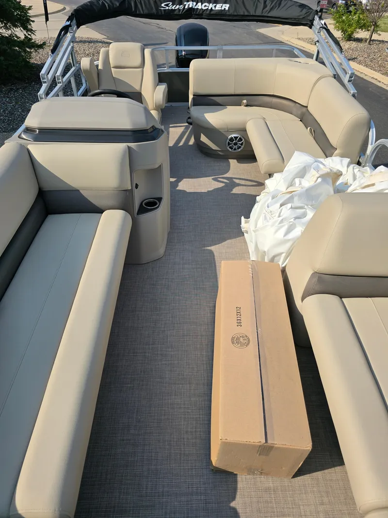 Slide: The Image of 2025 Sun Tracker Party Barge 18 DLX with beige seating and a cardboard box on deck. - 3