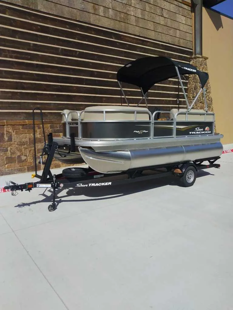 Slide: The Image of 2025 Sun Tracker Party Barge 16 DLX pontoon boat on trailer, parked outdoors. - 2