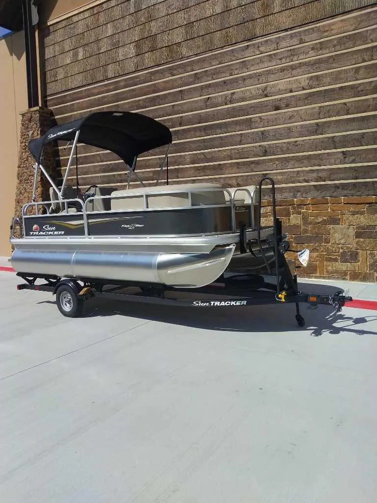 Slide: The Image of 2025 Sun Tracker Party Barge 16 DLX pontoon boat on trailer, parked outdoors. - 3