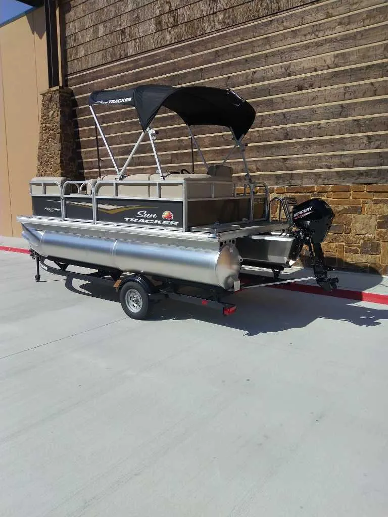 Slide: The Image of 2025 Sun Tracker Party Barge 16 DLX pontoon boat on trailer, parked outdoors. - 4