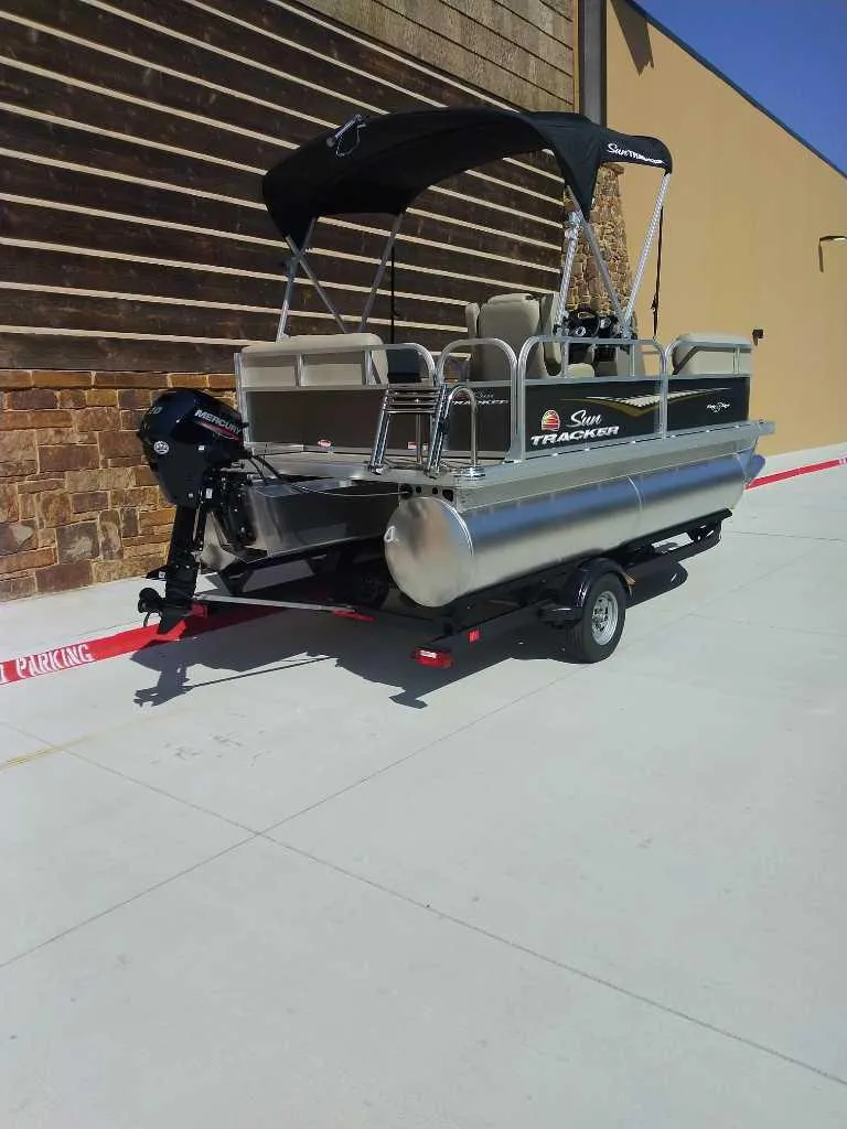 Slide: The Image of 2025 Sun Tracker Party Barge 16 DLX pontoon boat on trailer, parked outdoors. - 5