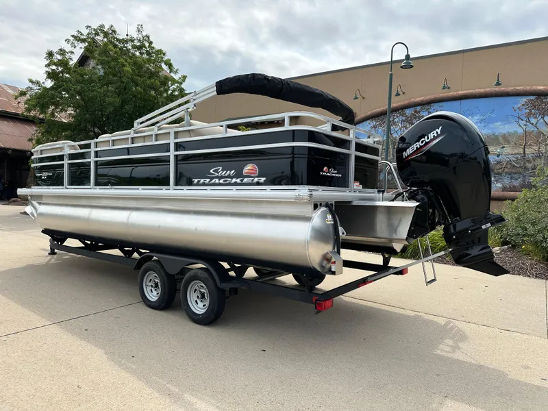 Slide: The Image of 2025 Sun Tracker SportFish 22 DLX pontoon boat on trailer, outdoor setting. - 2