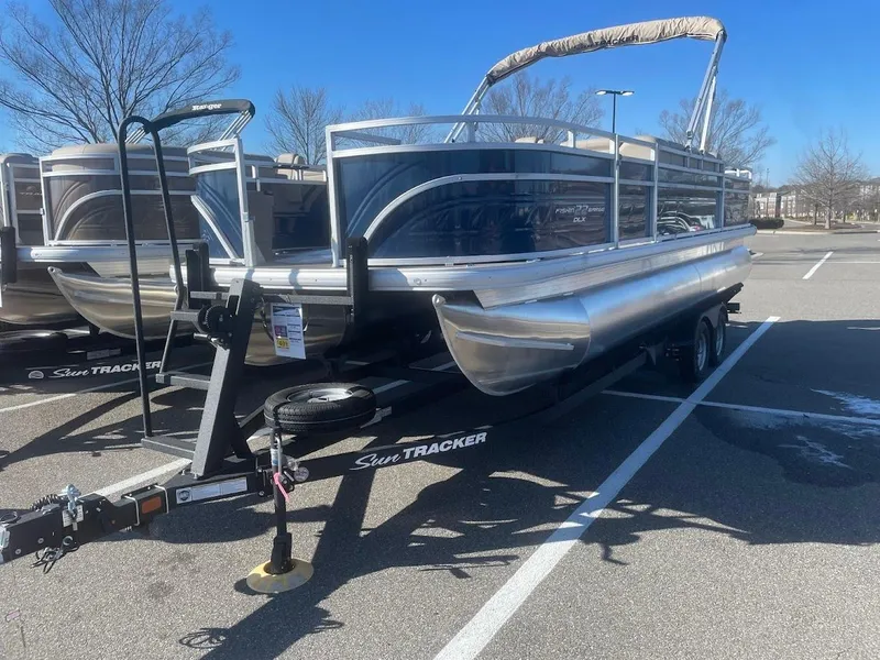 The Image of 2025 Sun Tracker Fishin' Barge 22 DLX pontoon boat on trailer in parking lot. - 0