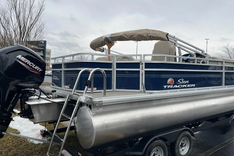 Slide: The Image of 2025 Sun Tracker Fishin' Barge 20 DLX pontoon boat on trailer, featuring Mercury outboard motor. - 2