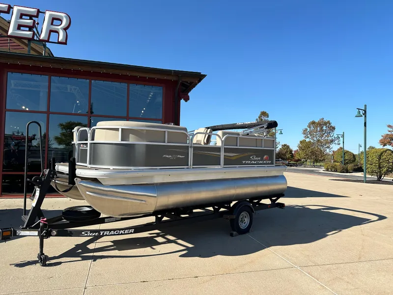Slide: The Image of 2025 Sun Tracker Party Barge 16 DLX pontoon boat on trailer, parked outside. - 5