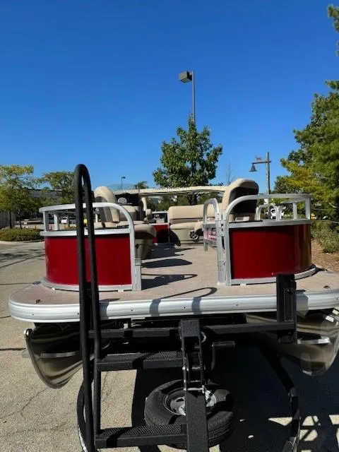 Slide: The Image of 2025 Sun Tracker Bass Buggy 16 XL Select pontoon boat on trailer, parked outdoors. - 2