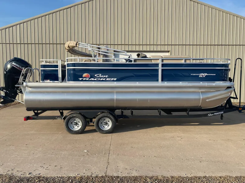 The Image of 2025 Sun Tracker Fishin' Barge 20 DLX pontoon boat on trailer, parked outdoors. - 0