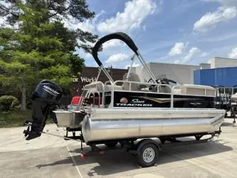 Slide: The Image of 2025 Sun Tracker Party Barge 16 DLX pontoon boat on trailer, outdoors. - 2
