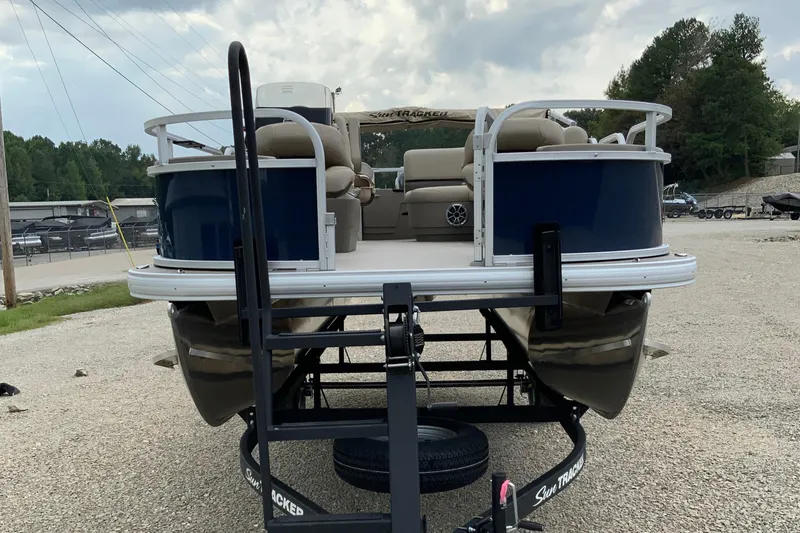 Slide: The Image of 2025 Sun Tracker Bass Buggy 18 DLX pontoon boat on a trailer, parked outdoors. - 13