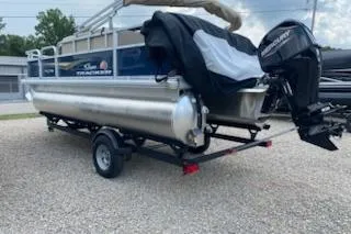 Slide: The Image of 2025 Sun Tracker Bass Buggy 18 DLX pontoon boat on trailer, parked on gravel. - 22