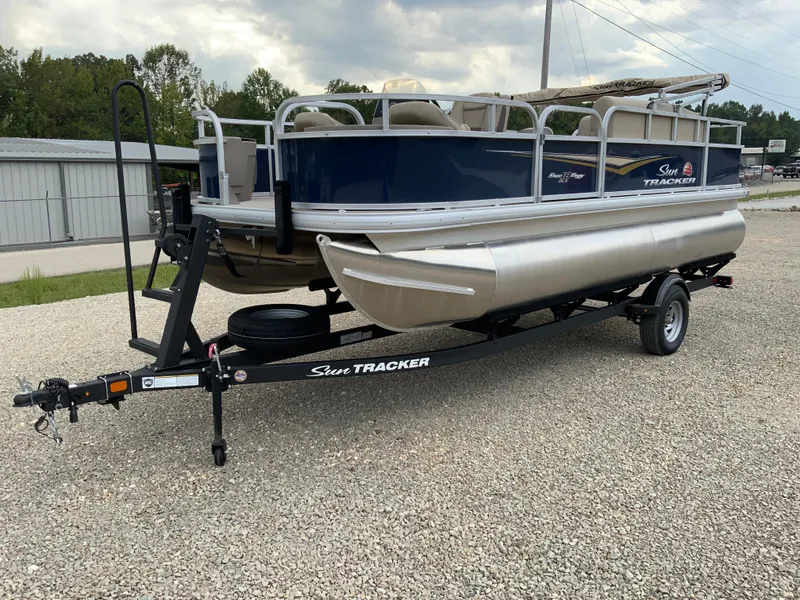 Slide: The Image of 2025 Sun Tracker Bass Buggy 18 DLX pontoon boat on trailer, parked on gravel. - 4