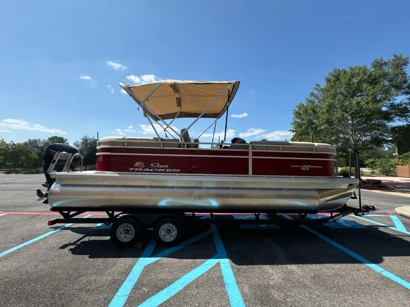 Slide: The Image of 2025 Sun Tracker Party Barge 22 DLX pontoon boat on trailer, parked outdoors. - 2
