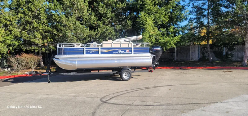 The Image of 2025 Sun Tracker Bass Buggy 18 DLX pontoon boat on trailer, parked outdoors. - 0