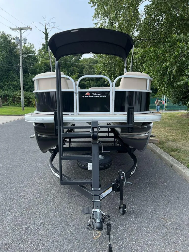 Slide: The Image of 2025 Sun Tracker Party Barge 16 DLX on trailer, parked on a road. - 2