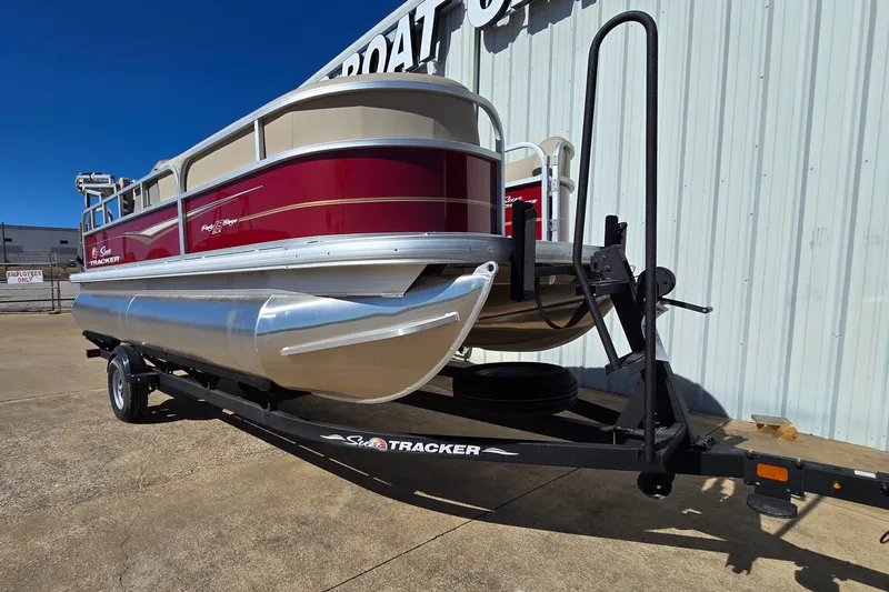 Slide: The Image of 2025 Sun Tracker Party Barge 18 DLX pontoon boat on trailer, parked outdoors. - 2