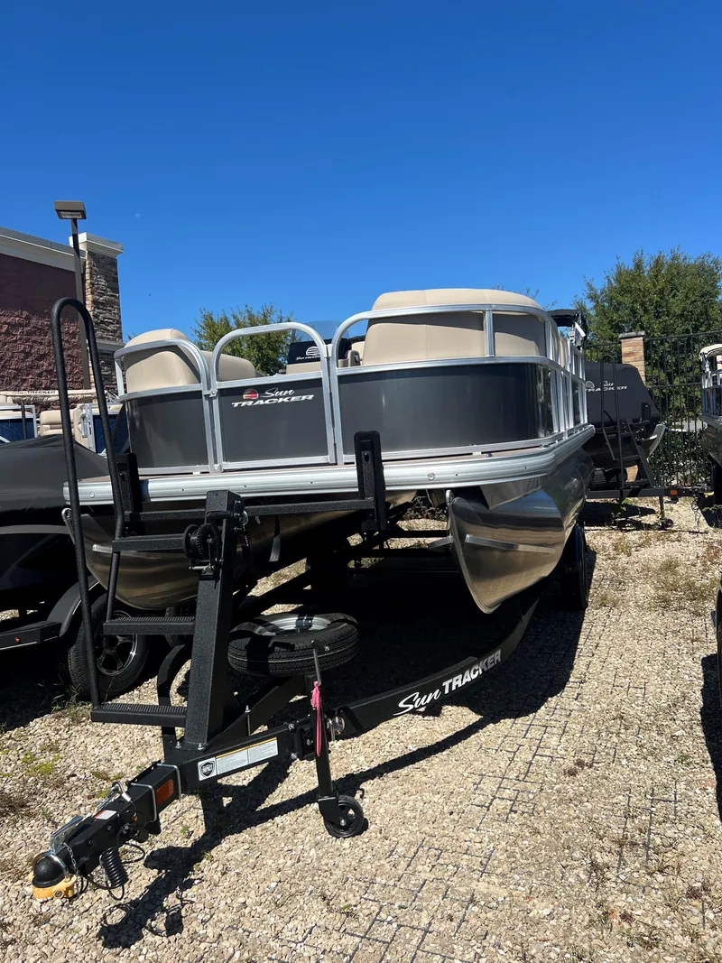 Slide: The Image of 2025 Sun Tracker Party Barge 16 DLX pontoon boat on trailer, parked outdoors. - 2