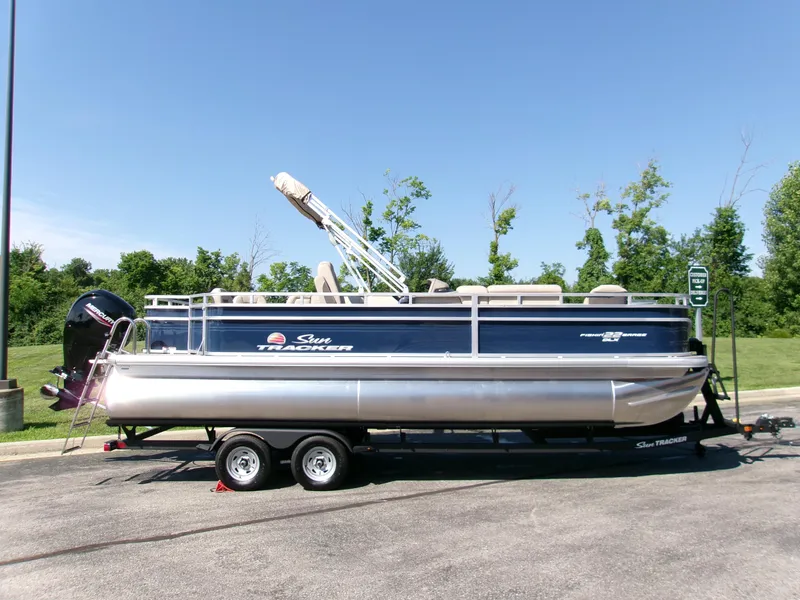 The Image of 2025 Sun Tracker Fishin' Barge 22 DLX pontoon boat on trailer, parked outdoors. - 0