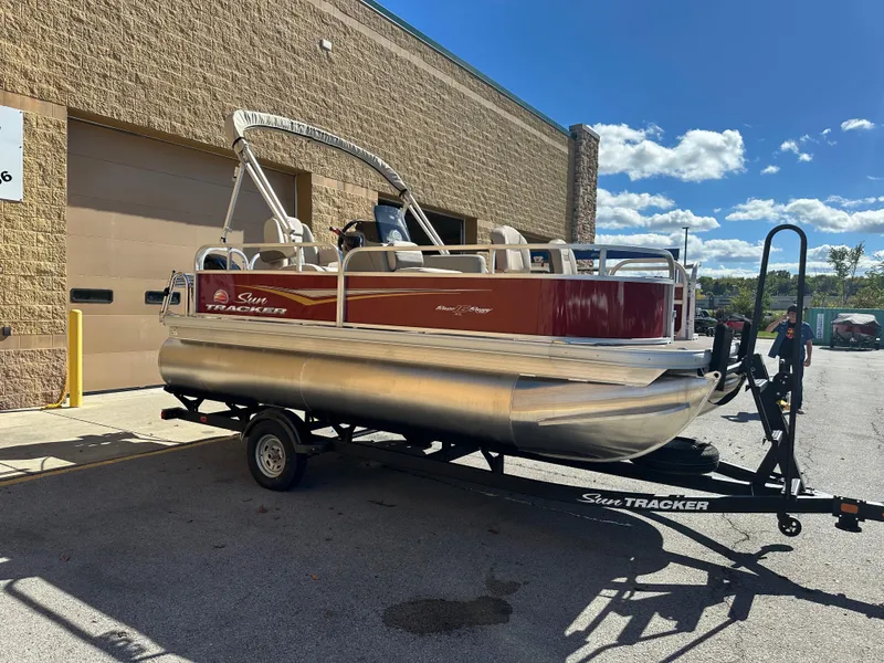 Slide: The Image of 2025 Sun Tracker Bass Buggy 16 XL Select pontoon boat on trailer, parked outdoors. - 3