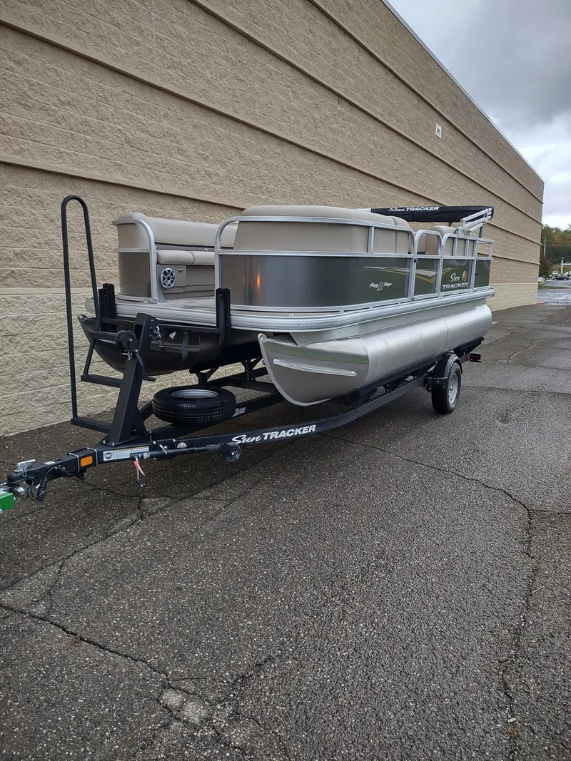 Slide: The Image of 2025 Sun Tracker Party Barge 18 DLX pontoon boat on trailer, parked outdoors. - 2