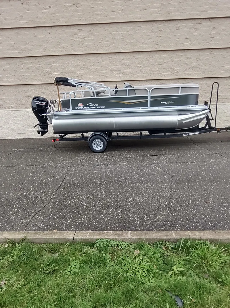 Slide: The Image of 2025 Sun Tracker Party Barge 18 DLX pontoon boat on trailer, parked outdoors. - 4