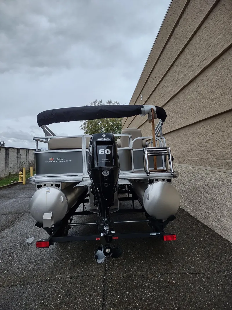 Slide: The Image of 2025 Sun Tracker Party Barge 18 DLX pontoon boat, rear view, parked outdoors. - 6