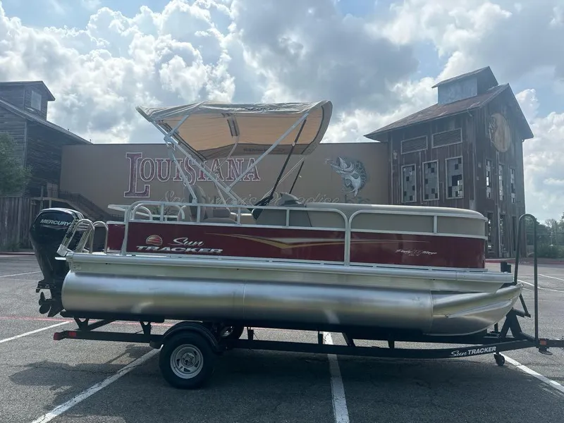 Slide: The Image of 2025 Sun Tracker Party Barge 18 DLX pontoon boat on trailer, parked outdoors. - 2