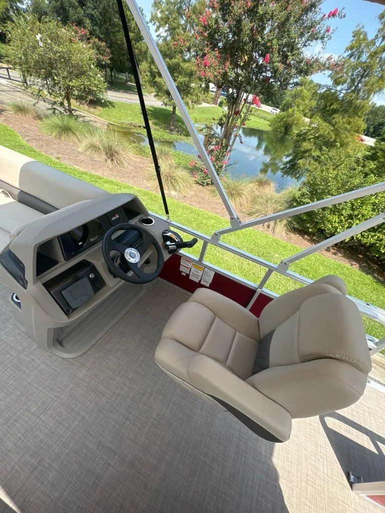 Slide: The Image of 2025 Sun Tracker Party Barge 18 DLX interior with steering wheel and seating, near scenic water view. - 6