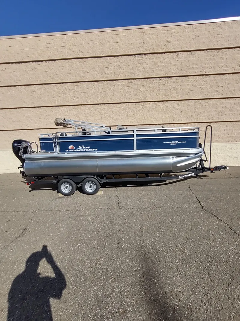 Slide: The Image of 2025 Sun Tracker Fishin' Barge 20 DLX pontoon boat on trailer, parked outdoors. - 4