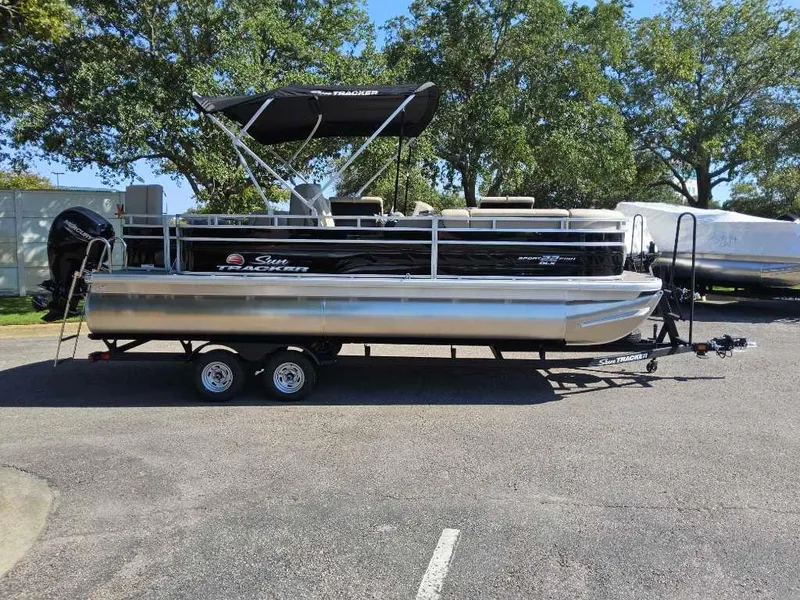 The Image of 2025 Sun Tracker SportFish 22 DLX pontoon boat on trailer, parked outdoors. - 0