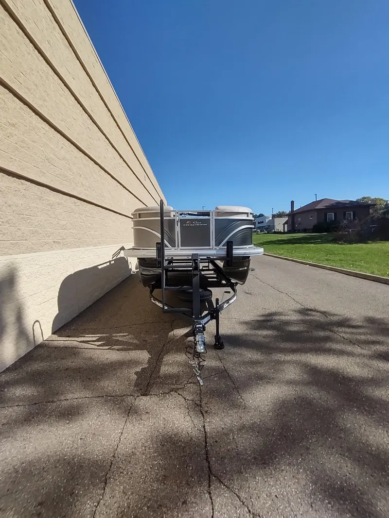 Slide: The Image of 2025 Sun Tracker Party Barge 22 RF DLX parked beside a building under clear blue sky. - 2
