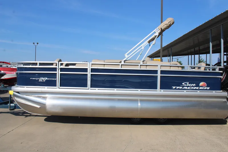 Slide: The Image of 2025 Sun Tracker Fishin' Barge 20 DLX pontoon boat docked under clear blue sky. - 2