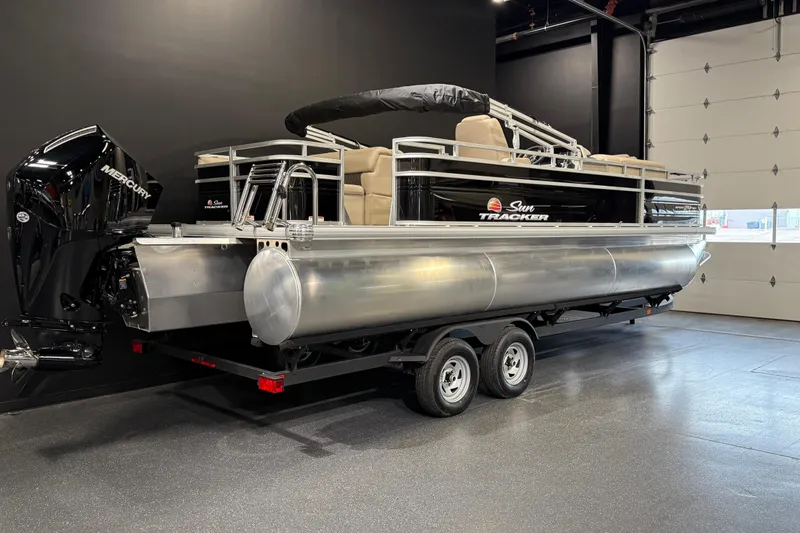 Slide: The Image of 2025 Sun Tracker Sportfish 24 XP3 pontoon boat in showroom, featuring Mercury outboard motor. - 2